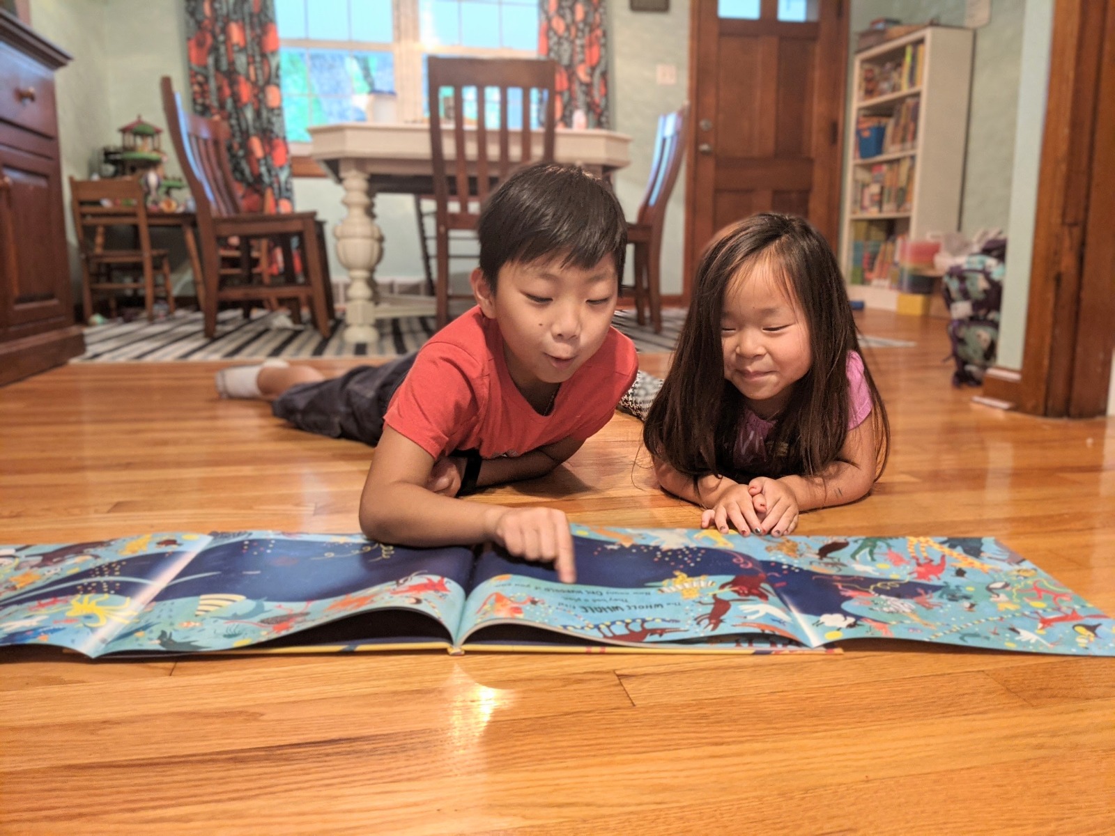 Two kids lay on the floor looking at a book