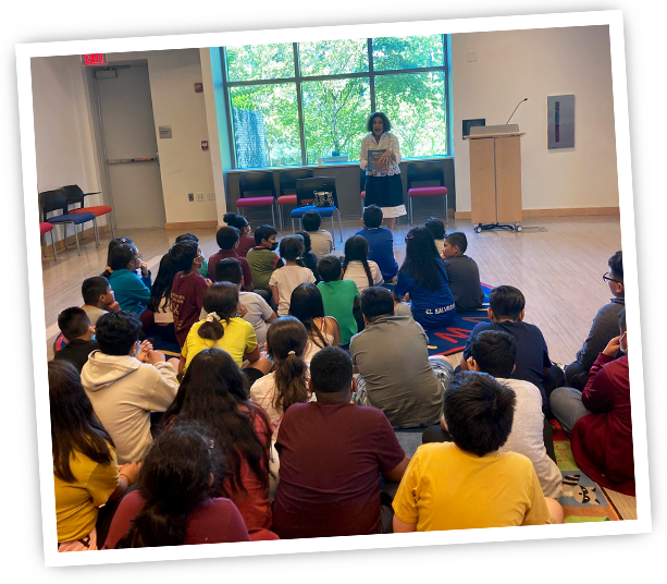 Wafa', author of Nour's Secret Library, holding her book and standing in front of a group of listening children