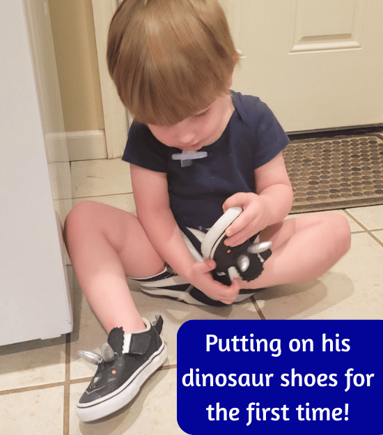 Picture of the author's child trying on his dinosaur shoes for the first time.