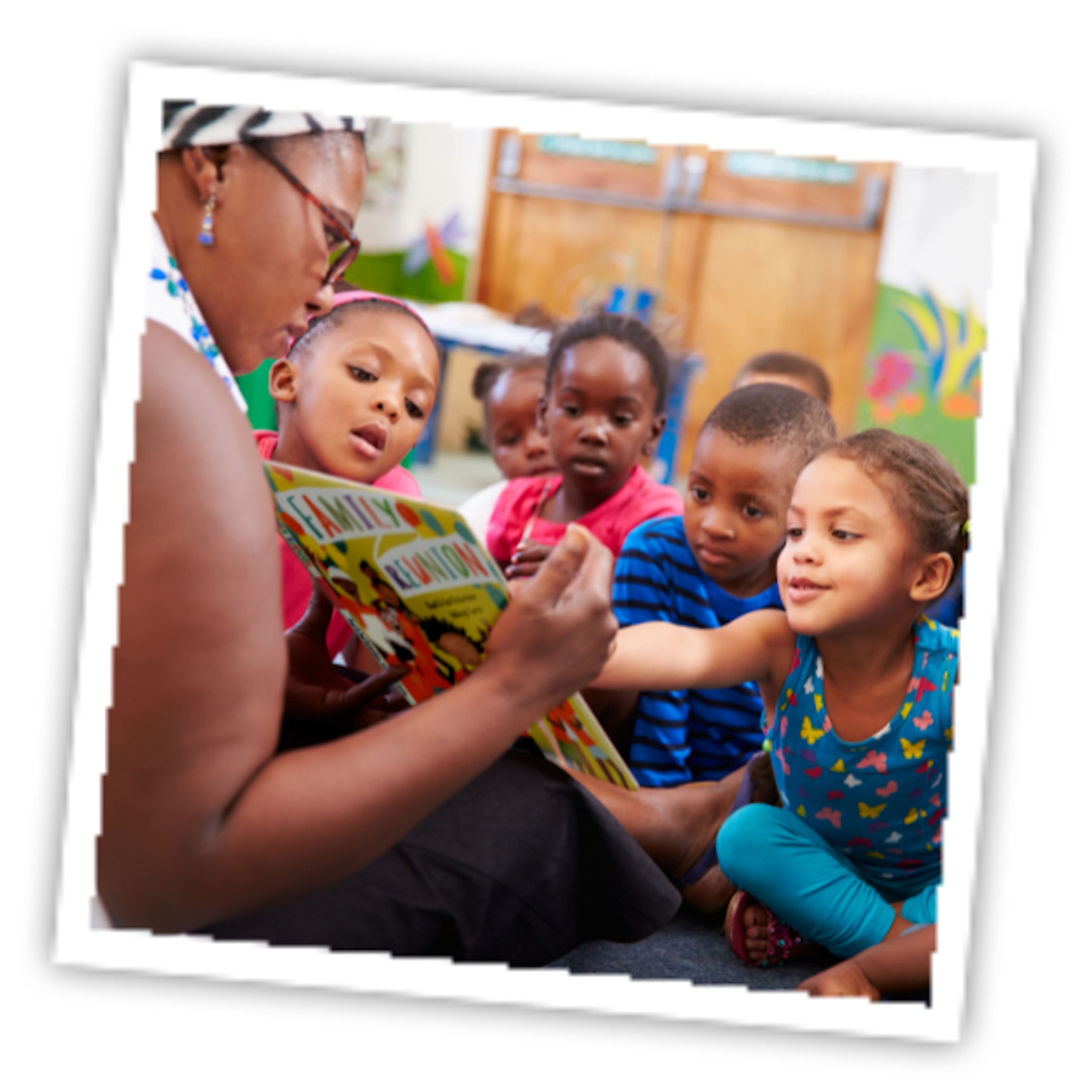 An adult reading a book to children sitting around her.